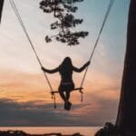 silhouette of person sitting on swing during sunset