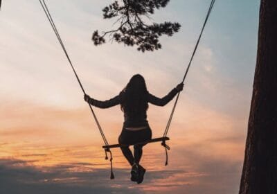 silhouette of person sitting on swing during sunset