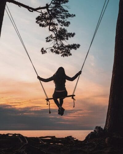 silhouette of person sitting on swing during sunset