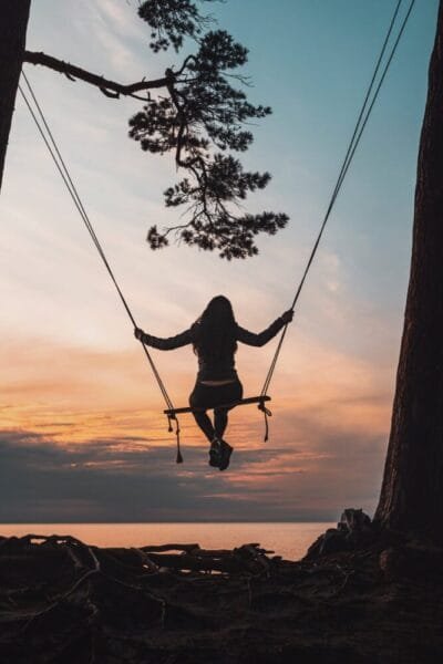 silhouette of person sitting on swing during sunset