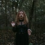 woman in black dress standing in the middle of a forest