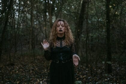 woman in black dress standing in the middle of a forest