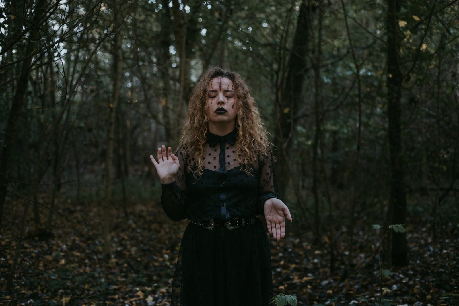 woman in black dress standing in the middle of a forest