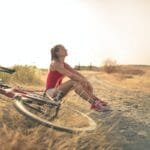 sportive woman with bicycle resting on countryside road in sunlight