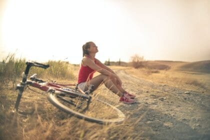 sportive woman with bicycle resting on countryside road in sunlight