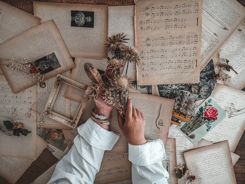Hands arranging dried flowers on antique papers with vintage sheet music in a creative flat lay. pitagoras, música de las esferas